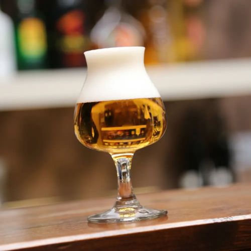 Filled beer glass Beer glass Specials Tasting 25 cl. in atmospheric setting, placed on wooden table.