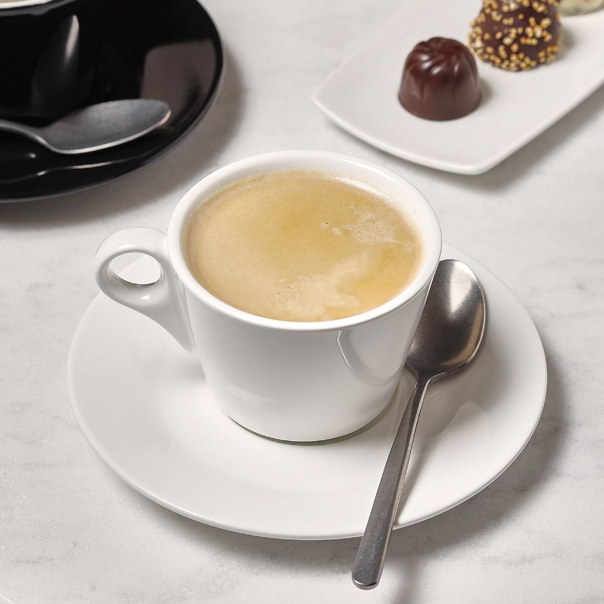 12.5 cm porcelain espresso dish with espresso and logo in atmospheric setting.